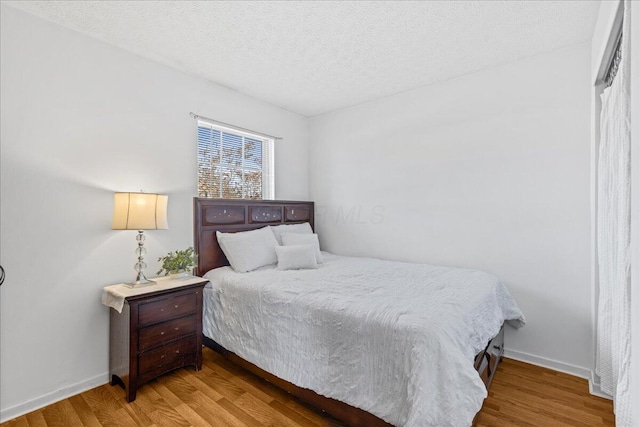 bedroom with wood finished floors, baseboards, and a textured ceiling