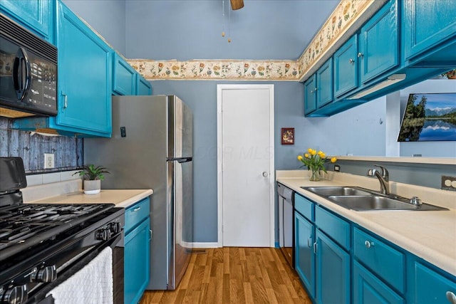 kitchen with light wood finished floors, blue cabinetry, light countertops, black appliances, and a sink