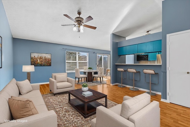 living room with a ceiling fan, wood finished floors, baseboards, and a textured ceiling