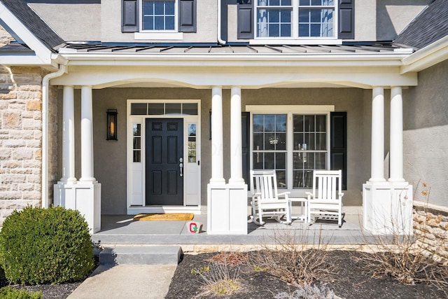 entrance to property with a standing seam roof, metal roof, covered porch, and stucco siding