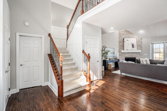 staircase with baseboards, high vaulted ceiling, hardwood / wood-style floors, and a fireplace