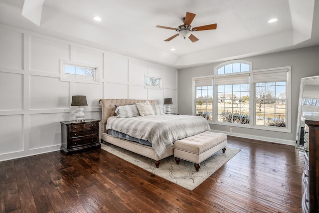 bedroom with dark wood finished floors, a tray ceiling, a decorative wall, and recessed lighting