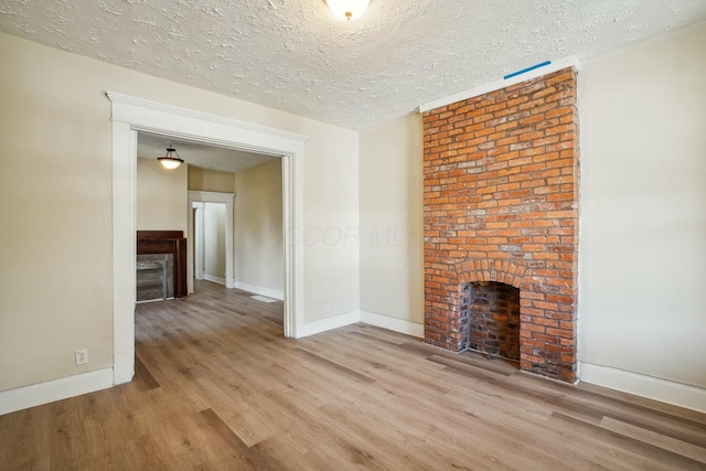 unfurnished living room featuring baseboards, a textured ceiling, wood finished floors, and a fireplace