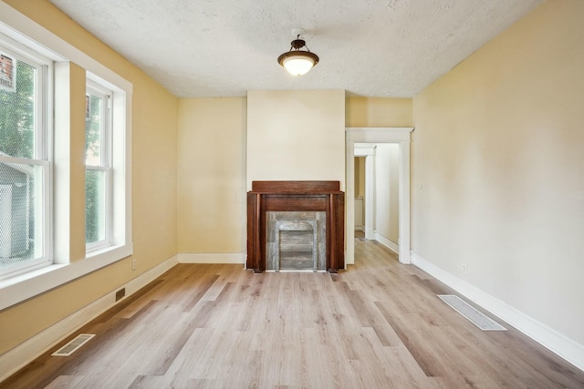 unfurnished living room with visible vents, a textured ceiling, baseboards, and wood finished floors