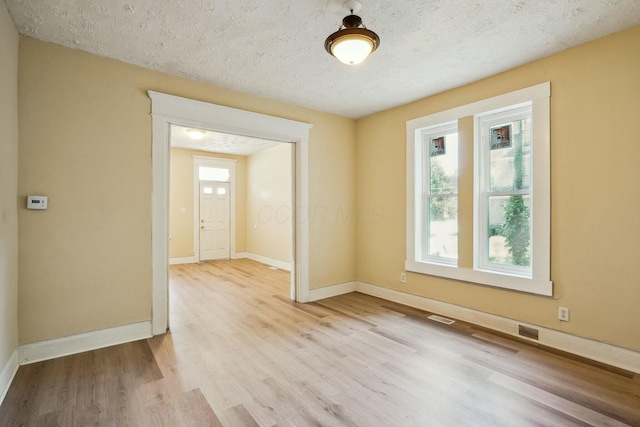 empty room featuring visible vents, a textured ceiling, baseboards, and wood finished floors