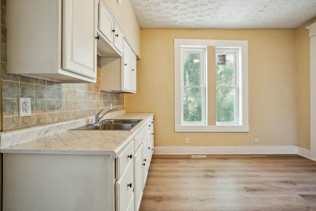 kitchen featuring light wood finished floors, baseboards, light countertops, decorative backsplash, and a sink