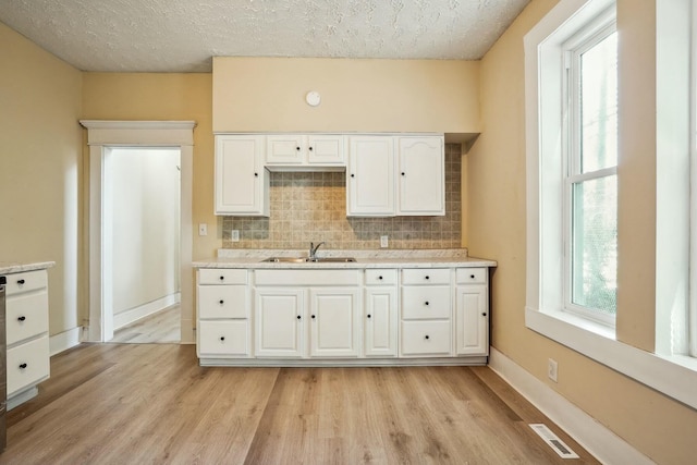 kitchen with visible vents, a sink, decorative backsplash, white cabinetry, and light wood-type flooring