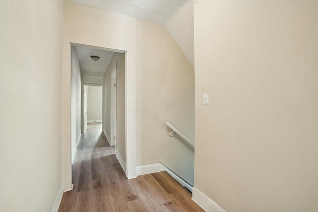 corridor featuring wood finished floors, an upstairs landing, baseboards, and vaulted ceiling