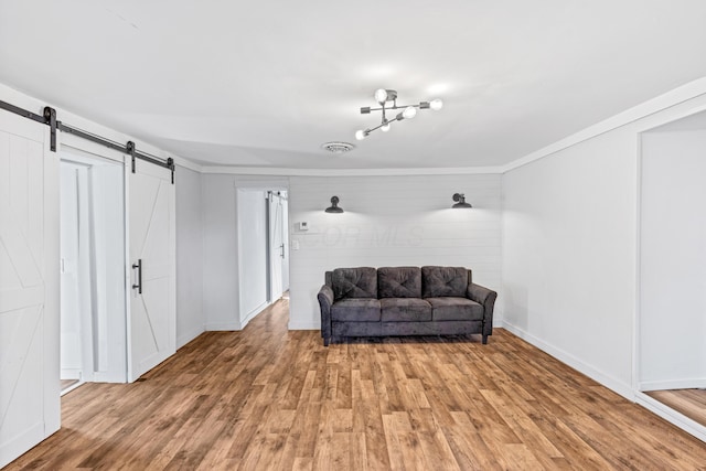 living area with visible vents, crown molding, baseboards, light wood-type flooring, and a barn door