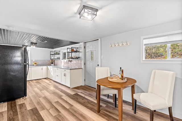 kitchen with decorative backsplash, white cabinetry, light wood-type flooring, and freestanding refrigerator