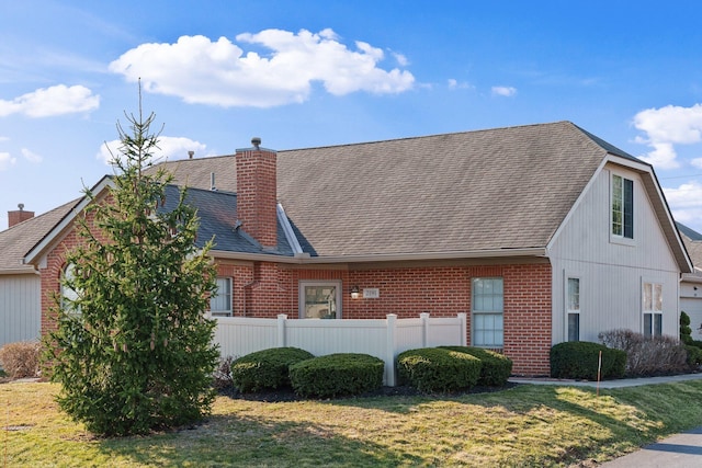 view of front facade with brick siding, roof with shingles, a chimney, and fence