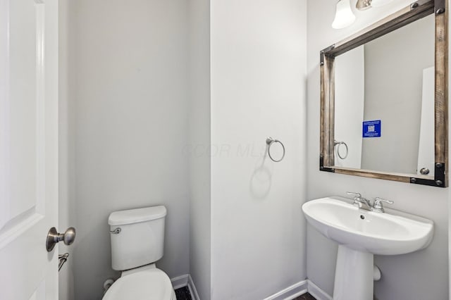 half bathroom with toilet, baseboards, and a sink