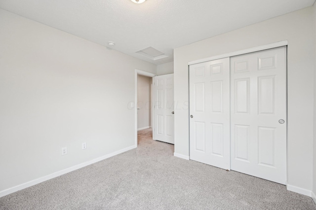 unfurnished bedroom featuring baseboards, a closet, attic access, and carpet