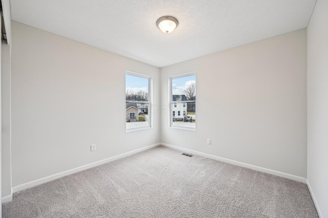 unfurnished room featuring baseboards, carpet floors, a textured ceiling, and visible vents