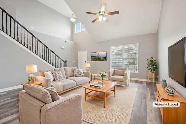 living room with stairway, plenty of natural light, wood finished floors, and a towering ceiling