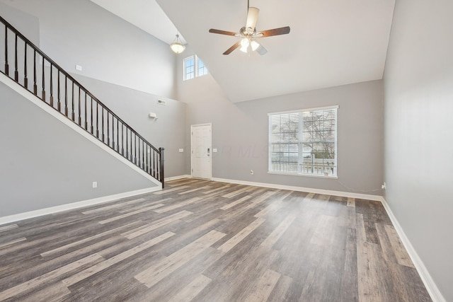 unfurnished living room featuring a towering ceiling, stairs, baseboards, and wood finished floors