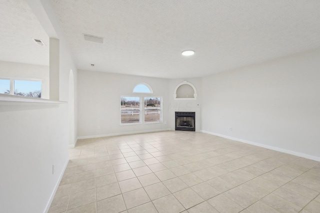 unfurnished living room with a tiled fireplace, visible vents, a textured ceiling, and baseboards