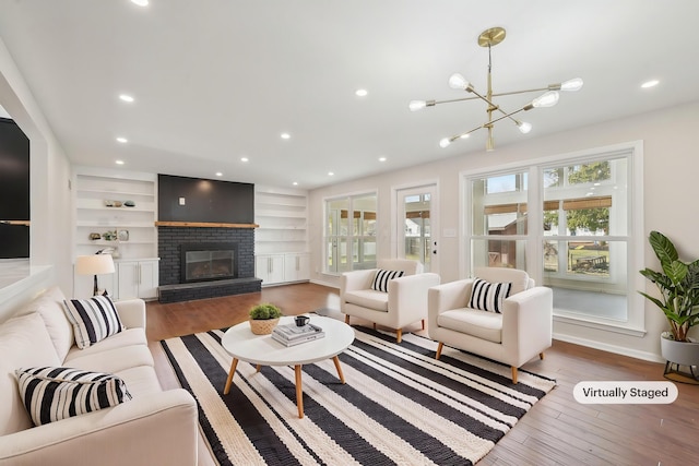 living room featuring built in features, wood finished floors, a fireplace, recessed lighting, and a chandelier