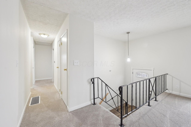 hallway with carpet, an upstairs landing, baseboards, and a textured ceiling