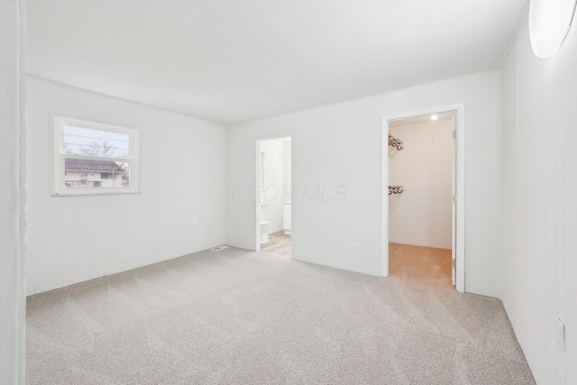 unfurnished bedroom with a spacious closet, carpet flooring, a closet, and ensuite bathroom