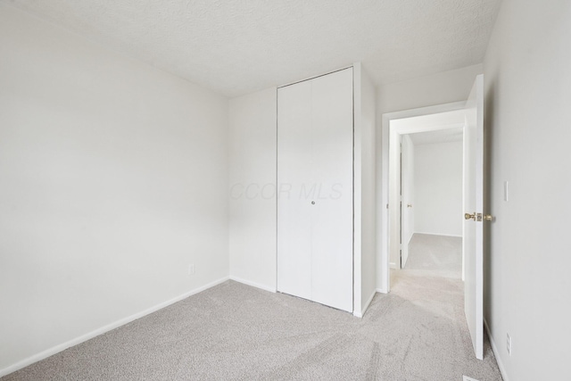 unfurnished bedroom with carpet flooring, baseboards, a closet, and a textured ceiling