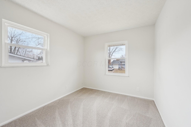 carpeted spare room featuring a textured ceiling and baseboards