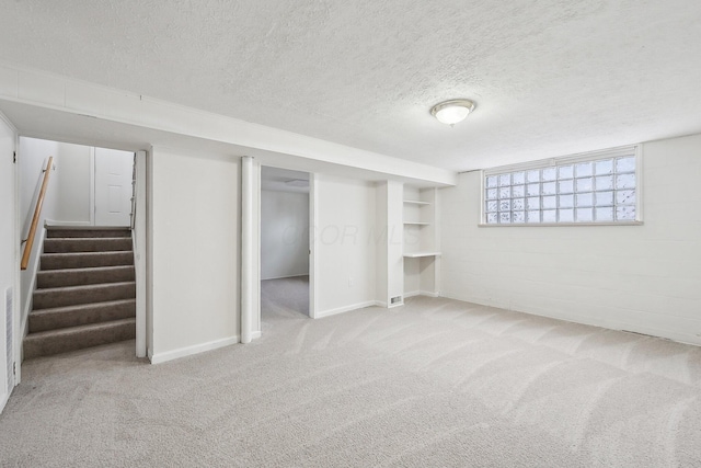 basement featuring concrete block wall, stairway, carpet flooring, and a textured ceiling