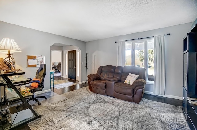 living room featuring baseboards, arched walkways, a textured ceiling, and wood finished floors