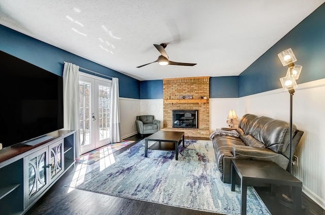 living area with wood finished floors, a fireplace, ceiling fan, french doors, and wainscoting