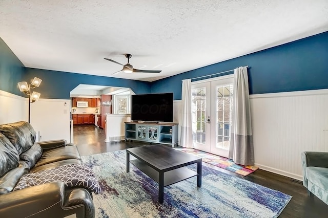 living area featuring french doors, wood finished floors, a textured ceiling, and a wainscoted wall