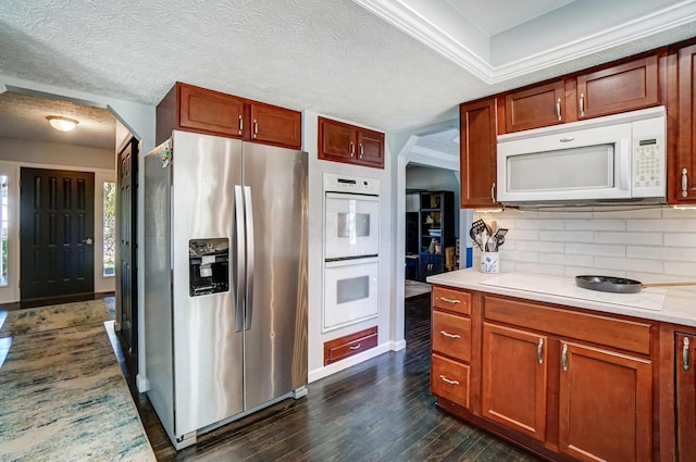 kitchen featuring tasteful backsplash, dark wood finished floors, white appliances, arched walkways, and light countertops