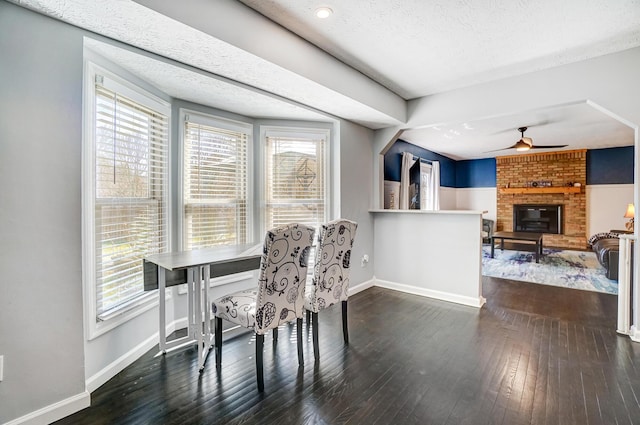 dining room with a fireplace, dark wood-type flooring, a ceiling fan, and baseboards