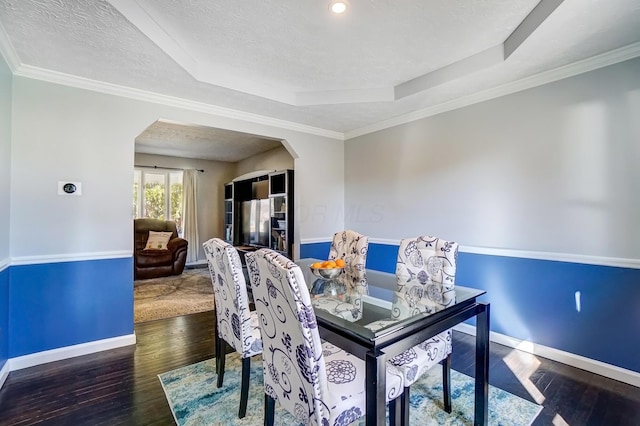 dining room with hardwood / wood-style floors, a raised ceiling, baseboards, and arched walkways