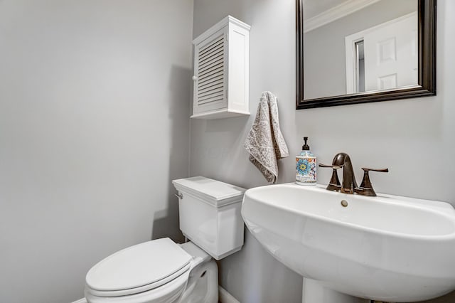 bathroom with toilet, crown molding, baseboards, and a sink