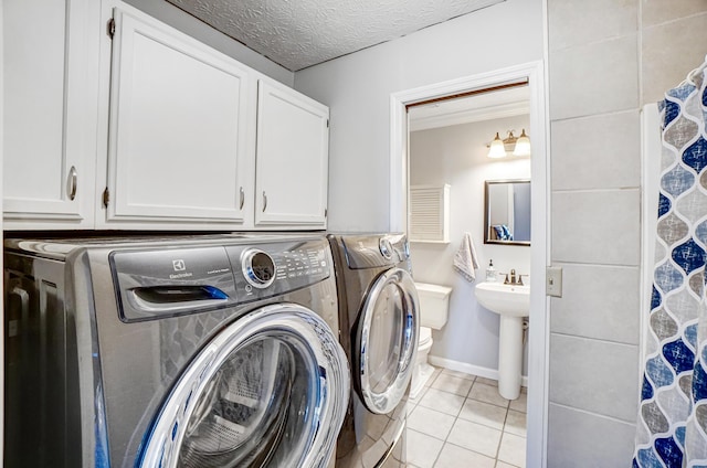 clothes washing area with washer and clothes dryer, light tile patterned flooring, cabinet space, a textured ceiling, and a sink