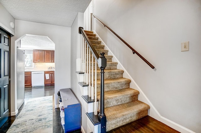 stairs featuring baseboards, wood finished floors, arched walkways, and a textured ceiling