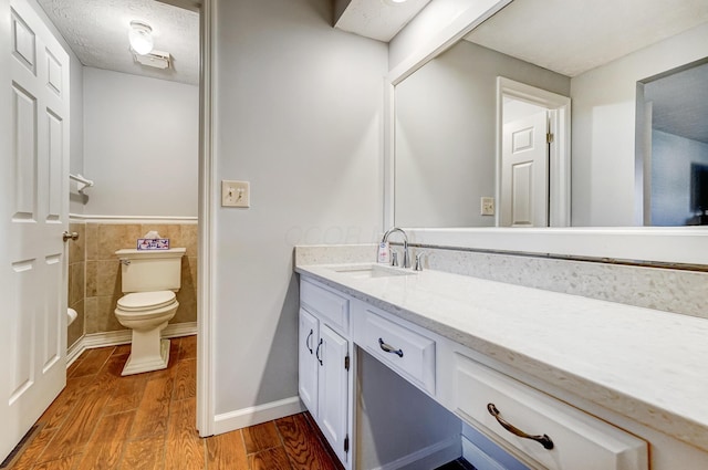 bathroom with tile walls, toilet, wood finished floors, a textured ceiling, and vanity