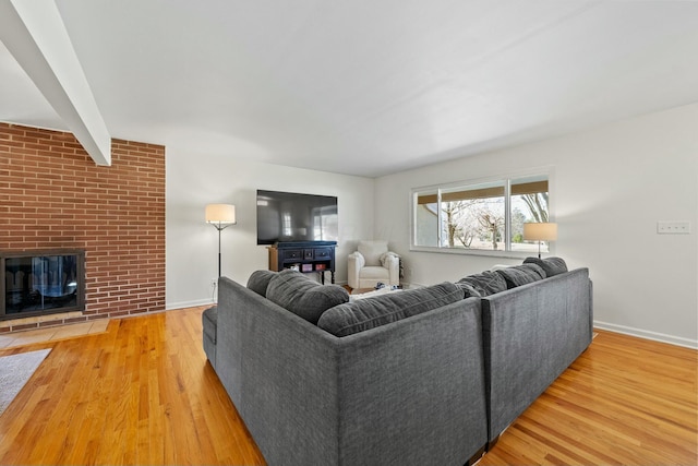 living room featuring beamed ceiling, a brick fireplace, baseboards, and wood finished floors