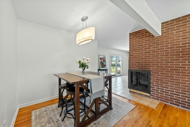 dining area with baseboards, brick wall, beam ceiling, a fireplace, and light wood-type flooring