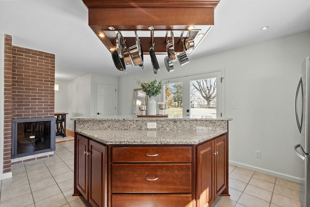 kitchen with light tile patterned floors, a brick fireplace, freestanding refrigerator, and light stone countertops