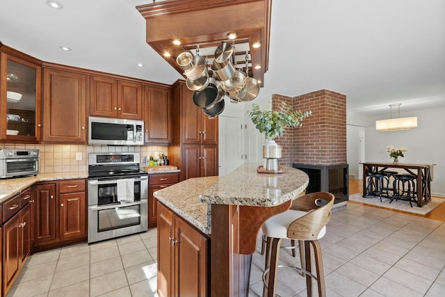 kitchen with glass insert cabinets, a kitchen bar, light tile patterned floors, decorative backsplash, and appliances with stainless steel finishes