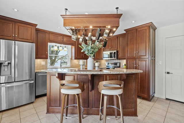 kitchen featuring light stone counters, a kitchen island, stainless steel appliances, light tile patterned floors, and decorative backsplash