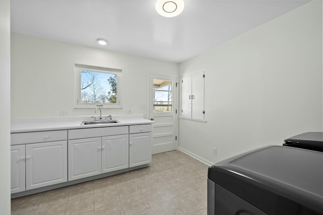 kitchen featuring baseboards, light countertops, washer / clothes dryer, white cabinetry, and a sink