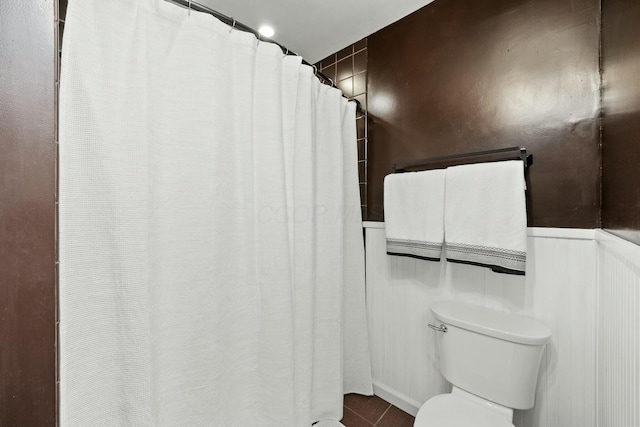 full bath featuring tile patterned flooring, a wainscoted wall, and toilet