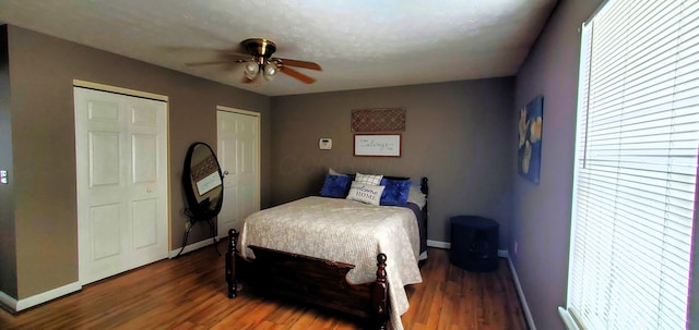 bedroom with ceiling fan, baseboards, multiple closets, and wood finished floors