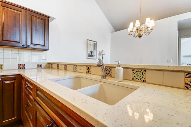 kitchen with a notable chandelier, lofted ceiling, a sink, decorative backsplash, and light stone countertops