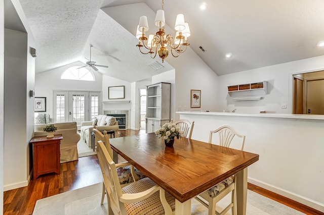 dining room with visible vents, vaulted ceiling, ceiling fan with notable chandelier, a tile fireplace, and wood finished floors