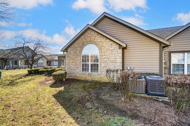 view of home's exterior featuring stone siding, central AC unit, and a yard