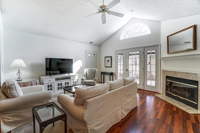 living area featuring high vaulted ceiling, a ceiling fan, a tiled fireplace, a textured ceiling, and wood finished floors