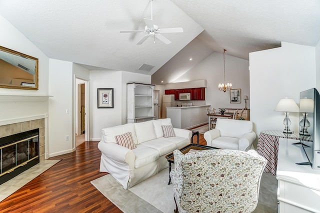 living area with ceiling fan with notable chandelier, wood finished floors, a fireplace, baseboards, and vaulted ceiling